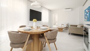 Ein moderner Essbereich mit einem runden Holztisch, vier Stühlen, einer Blumenvase und einem großen Flachbildfernseher an der Wand.