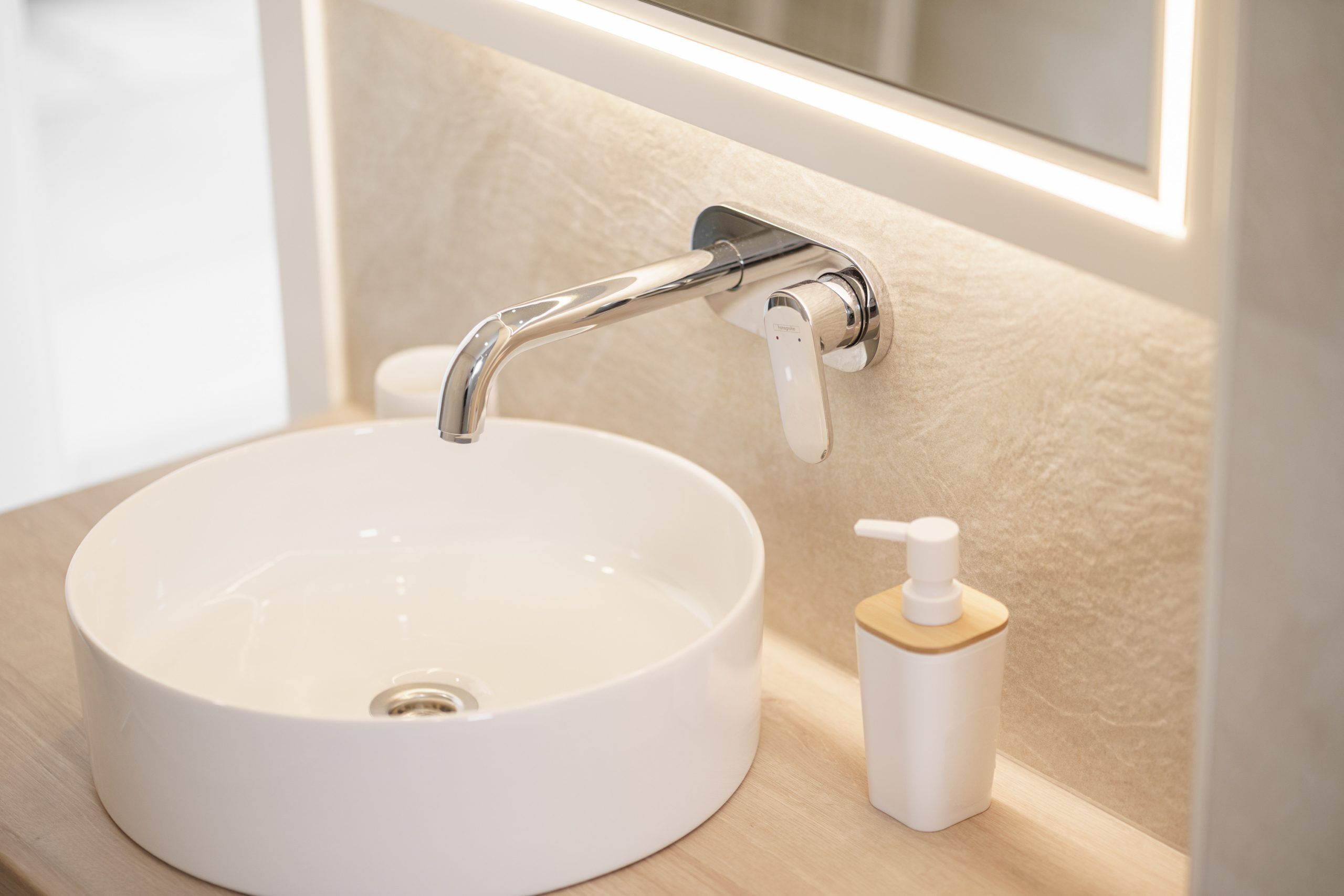 Un évier blanc avec un robinet chromé, un distributeur de savon et un miroir au-dessus de l’évier.
