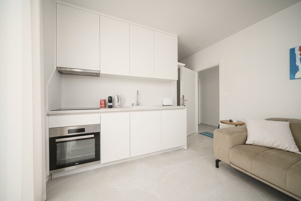 A modern kitchen with white cabinetry, a built-in oven, and a dining area with a beige sofa. - Apartments Bianca Vodice (Vodice)