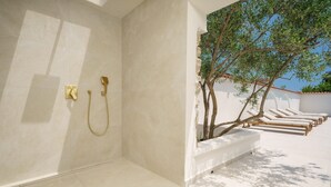 Ein modernes Badezimmer mit weißen Fliesen, einer goldfarbenen Duschbrause und einem Baum im Hintergrund.