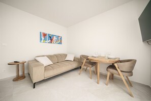 Ein modernes Wohnzimmer mit einem beige gefärbten Sofa, zwei Sesseln, einem kleinen Holztisch und einem Gemälde an der Wand.