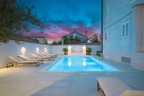 A swimming pool with lounge chairs, a white building with shutters, and a sunset sky. - Apartments Bianca Vodice (Vodice)