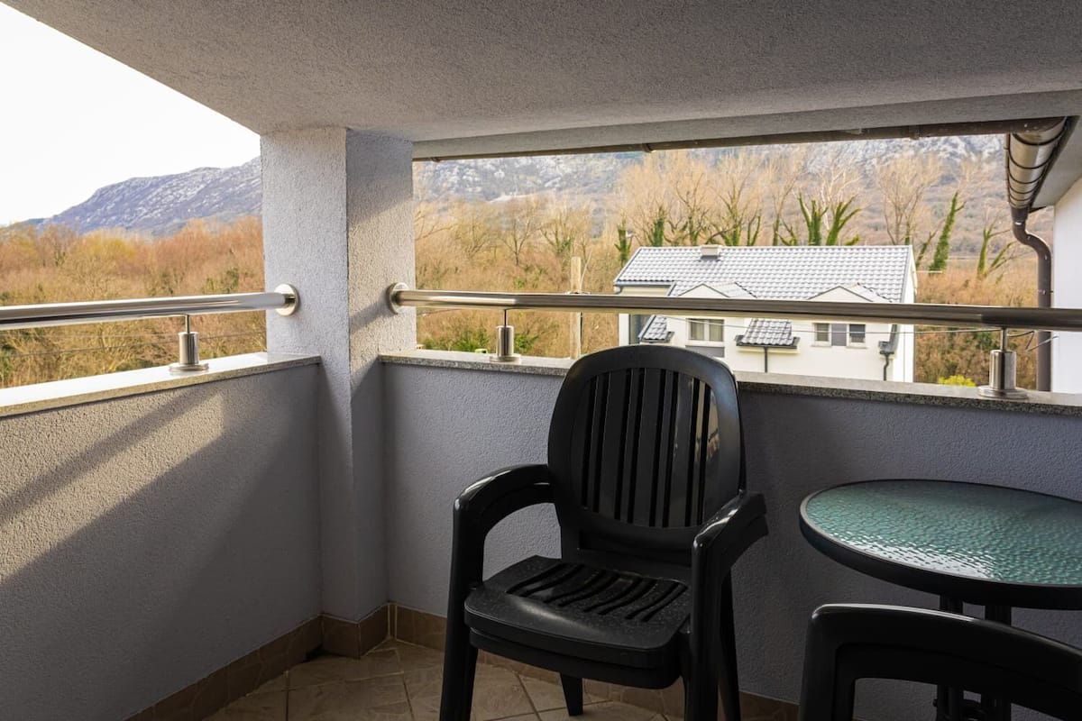 Un balcón con vistas a las montañas, una silla y una mesita.