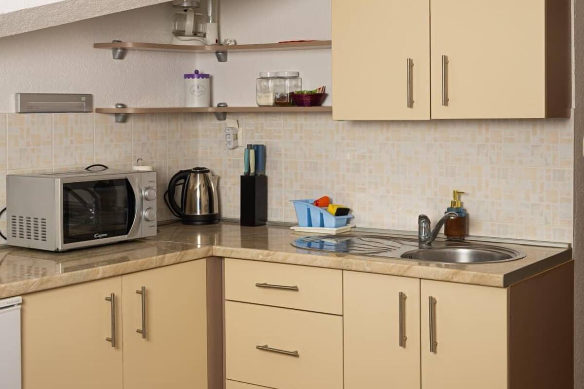 Una cocina compacta con microondas, hervidor y pileta.