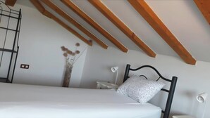 Une chambre à coucher avec un lit, une table de chevet, une lampe, un vase décoratif et des poutres en bois au plafond.