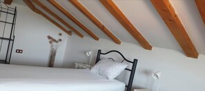A bedroom with a bed, a nightstand, a lamp, a decorative vase, and wooden beams on the ceiling. - Apartment Adri (Rovinj)