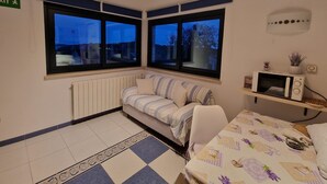 Une chambre avec un lit, une petite table, un four à micro-ondes et deux fenêtres donnant sur l’extérieur.