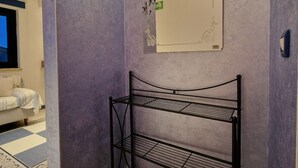 Un coin de pièce avec une étagère en métal, un miroir fixé au mur et un tapis à motifs.