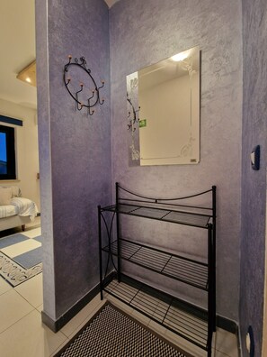 A corner of a room with a metal shelf unit, a wall-mounted mirror, and a patterned rug. - Apartment Adri (Rovinj)