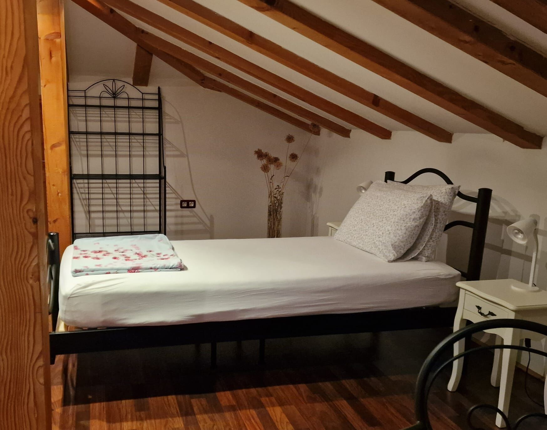 Un dormitorio con una cama, una mesita de noche, una lámpara, una silla y techo de madera.