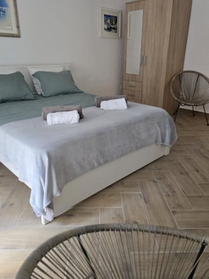 Ein Schlafzimmer mit Bett, Kissen, einem Kleiderschrank, einem Sessel und einem Bild an der Wand.