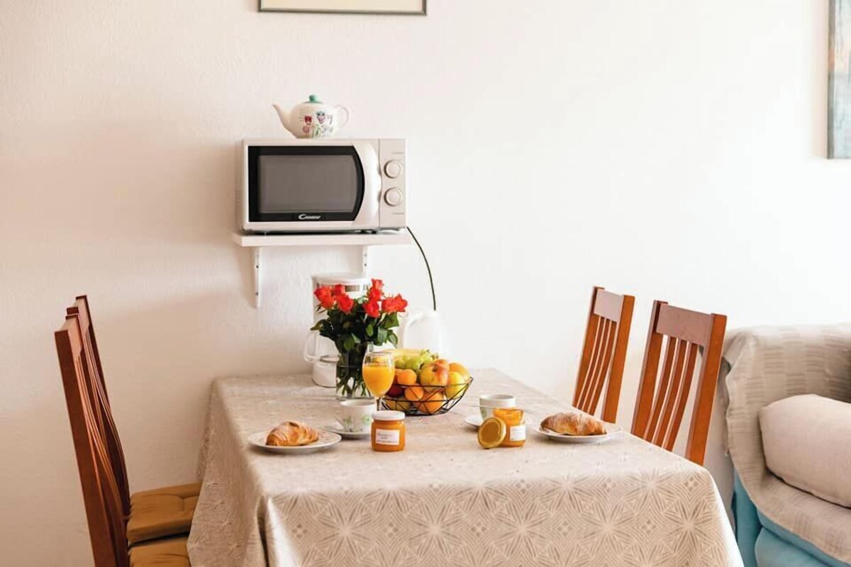Ein Frühstücksbuffet mit Tisch, Stühlen, einer Mikrowelle, einem Teekessel, einer Obstschale und einer Kaffeemaschine.