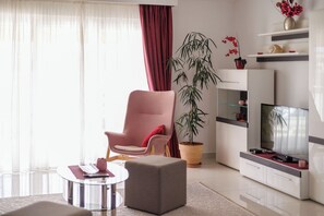 A modern living room with a large flat-screen TV, a pink armchair, a potted plant, and a small round table. - Apartments Villa Marija (Seget)