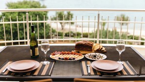 A dining table set with plates, cutlery, a bottle of wine, and a loaf of bread, overlooking a body of water with boats. - Apartments Villa Marija (Seget)