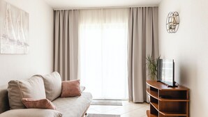 A living room with a sofa, a television on a wooden stand, and a window with curtains. - Apartments Villa Marija (Seget)