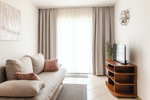 Ein Wohnzimmer mit einer Couch, einem Fernseher auf einem Holzboden und einem Fenster mit Vorhängen.