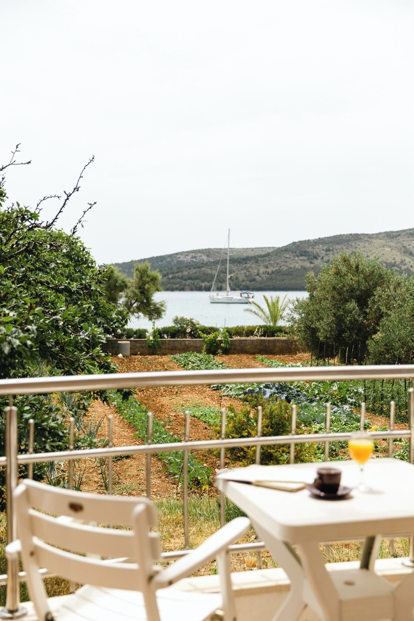 A terrace with a table and chairs, overlooking a body of water and a sailboat.