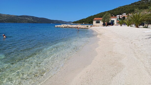 A beach with clear water, a rocky breakwater, and a building with a red roof. - Apartments Villa Marija (Seget)