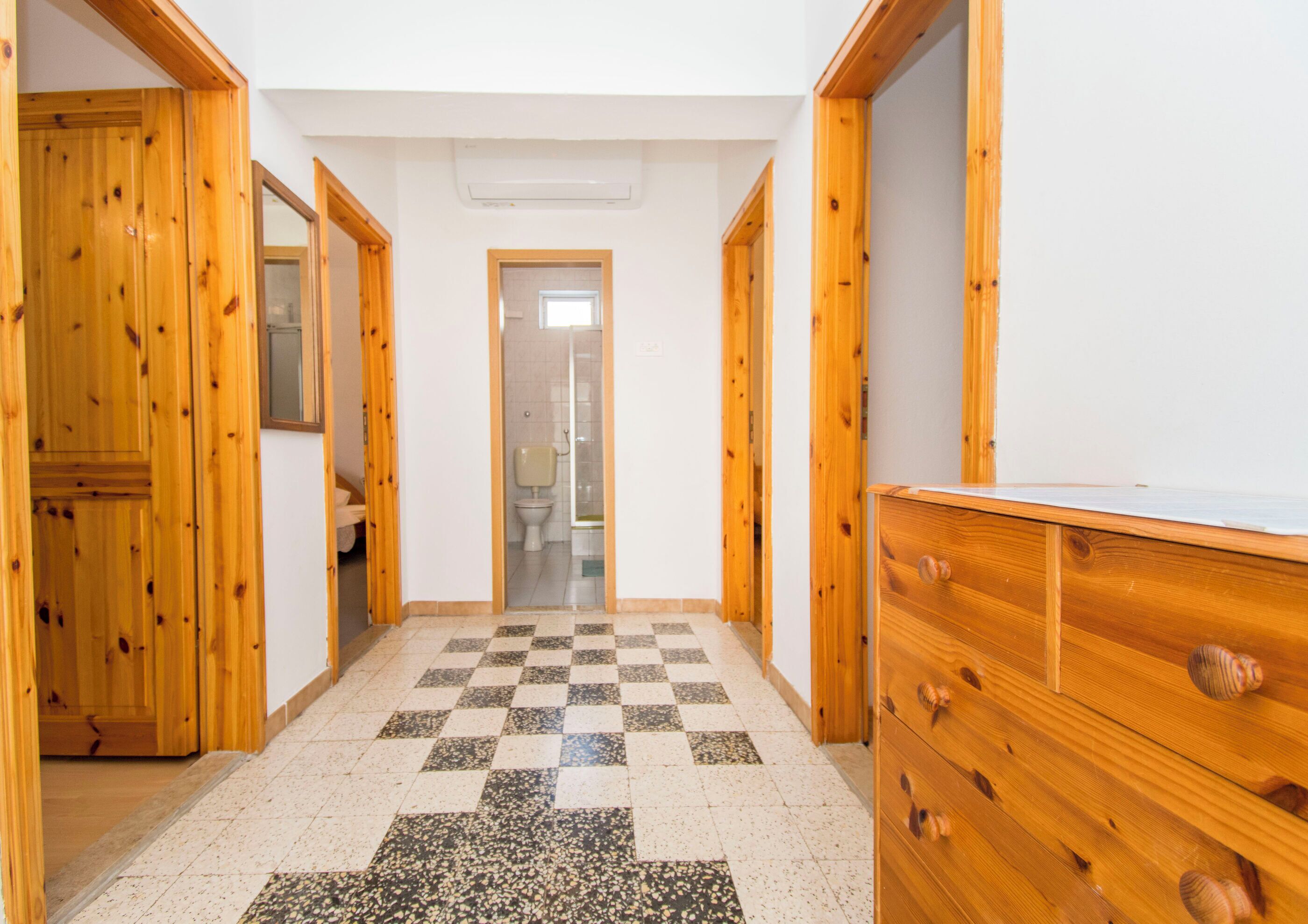 A hallway with wooden doors, a checkered floor, and a view into a bathroom.