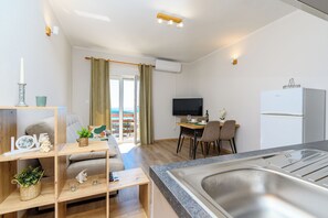 A modern kitchen with a built-in sink, a dining area with a table and chairs, a flat-screen TV, and a view of the outdoors. - Apartments Andrija (Rab)
