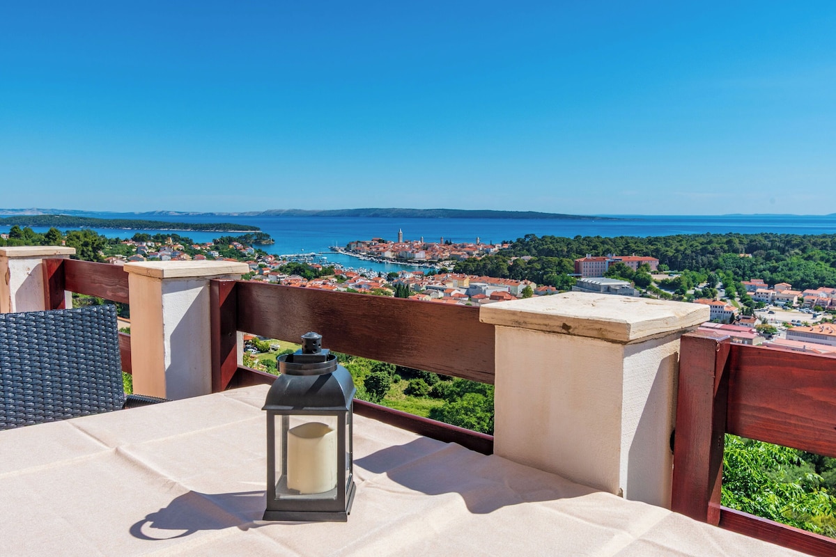 A balcony with a table, a lantern, and a view of a coastal town.
