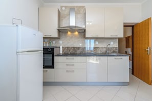 A modern kitchen with white cabinets, a stainless steel range hood, and a built-in oven. - Apartments Andrija (Rab)