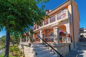 A two-story building with a stone facade, a balcony with a metal railing, and a staircase leading to the entrance. - Apartments Andrija (Rab)