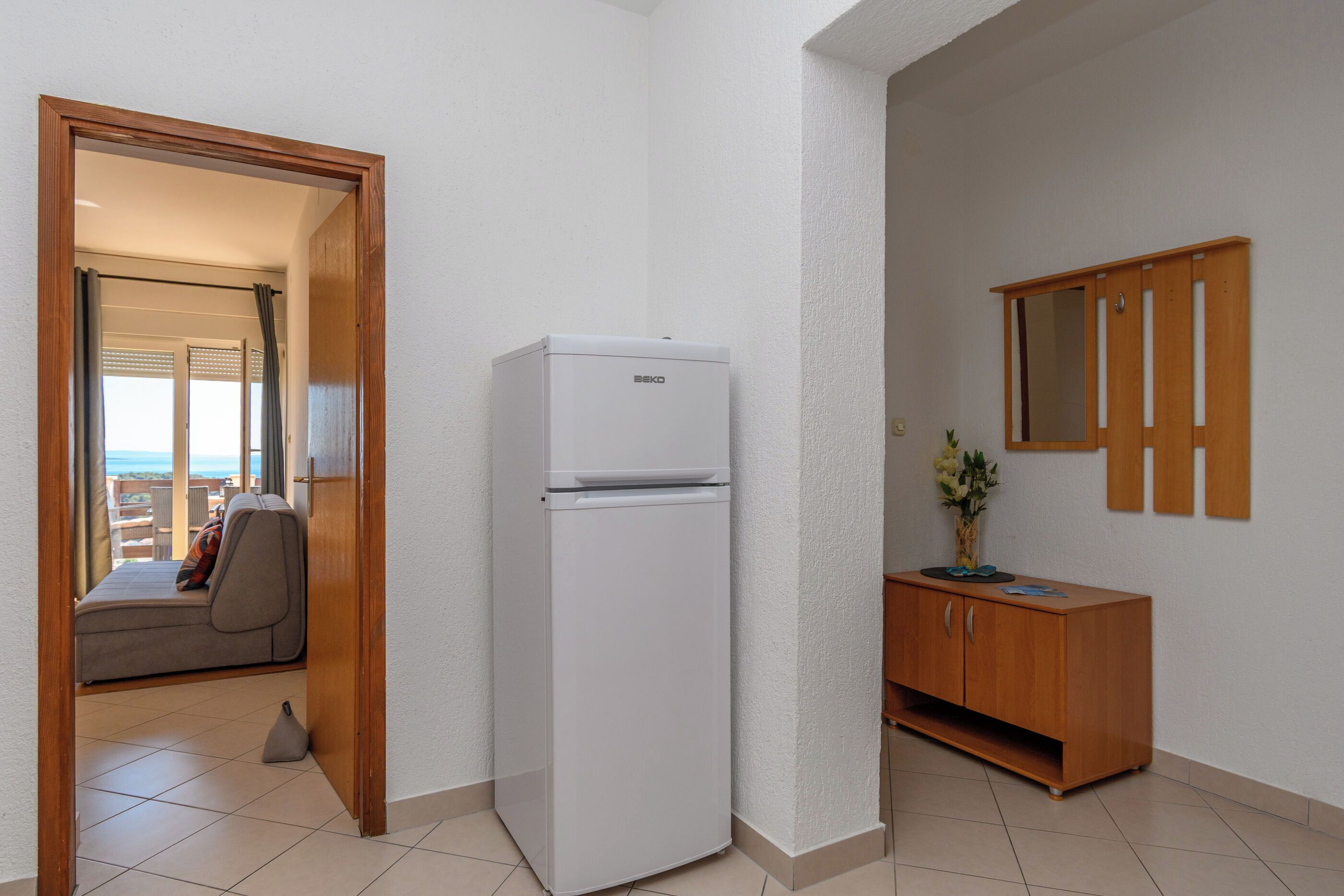 A compact room with a white refrigerator, a wooden cabinet, and a door leading to a balcony with a view.