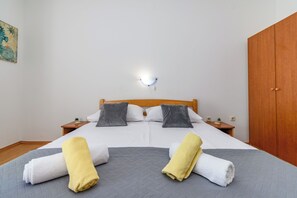 A neatly made bed with two pillows, a bedside table with a lamp, and a wooden wardrobe. - Apartments Andrija (Rab)