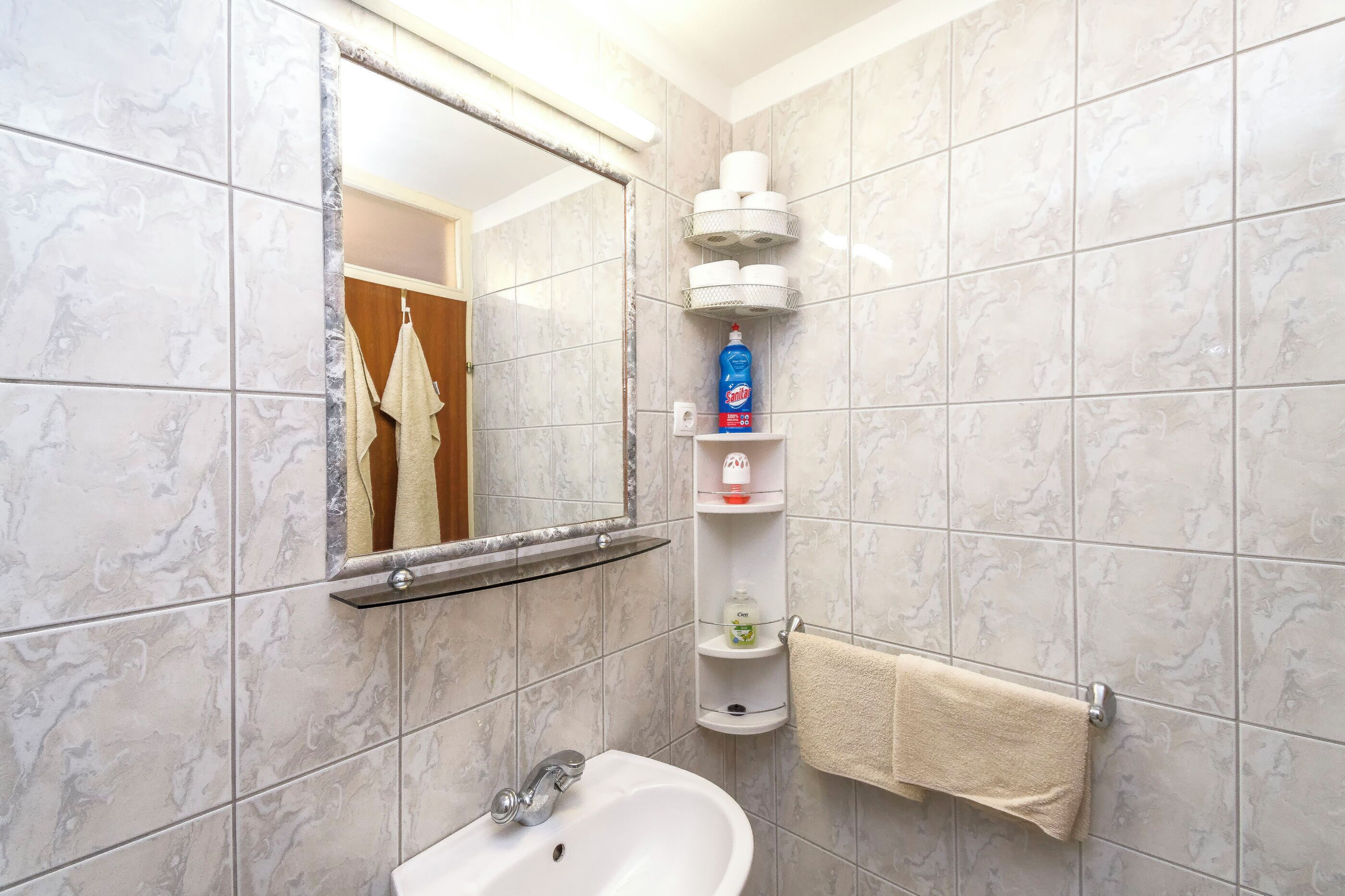 Un baño con lavamanos blanco, un espejo y un estante con artículos de aseo.