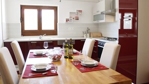 A dining area with a wooden table set for four, a window with a view, and a kitchen with red cabinets and white appliances. - Apartment Feelgood (Benkovac)