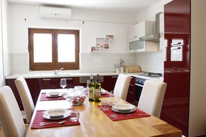 Ein Essbereich mit Holztisch, gedeckt für vier Personen, ein Fenster mit Aussicht und eine Küche mit roten Schränken und weißen Geräten.