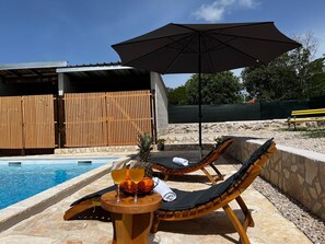 Ein Poolbereich mit Liegestühlen, einem Tisch mit Getränken und einem Sonnenschirm.