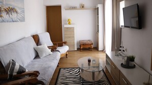 A living room with a sofa, a glass coffee table, a zebra rug, a wooden bench, a TV, and a painting of a lighthouse. - Apartment Feelgood (Benkovac)