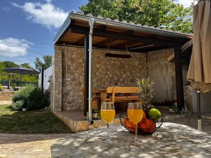 A stone building with a wooden deck, outdoor seating, and a table with drinks and fruit. - Apartment Feelgood (Benkovac)