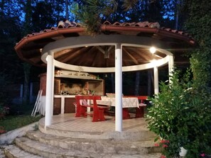 A covered outdoor dining area with a brick fireplace, wooden tables, and a white railing. - Apartment Villa Zizi (Viskovo)