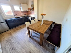 A modern kitchen with black cabinets, a wooden dining table, and a vase with flowers. - House Beachfront Delight (Pasman)