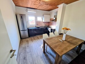 A modern kitchen with black cabinets, a stainless steel refrigerator, and a wooden dining table with a vase of sunflowers. - House Beachfront Delight (Pasman)