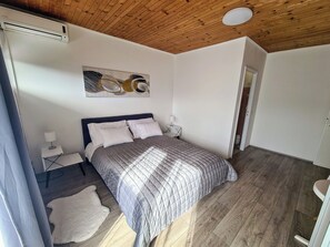 A bedroom with a wooden ceiling, a bed with a quilted blanket, a white rug, and a painting on the wall. - House Beachfront Delight (Pasman)