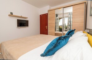 A bedroom with a bed, a TV, a wardrobe, and a window with a view. - Apartments Zlatka (Okrug)