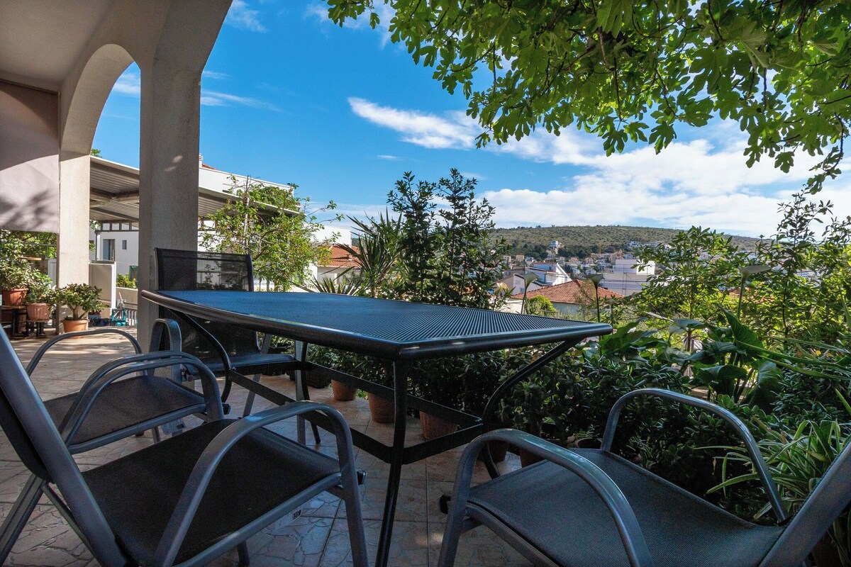 A table and chairs set outdoors with a view of a town and hills in the background.