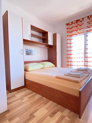 Ein Schlafzimmer mit einem hölzernen Bett, eingebauten Stauraum, einem Fenster mit Vorhängen und einem Holzboden.