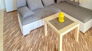 A modern living room with a sofa, a coffee table, a ceiling fan, and a kitchen area in the background. - Apartments Mia (Crikvenica)
