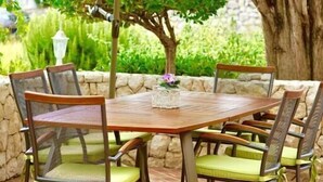 A round wooden table with six chairs, an umbrella, and a stone wall in the background. - Apartment Ljubica (Rab)