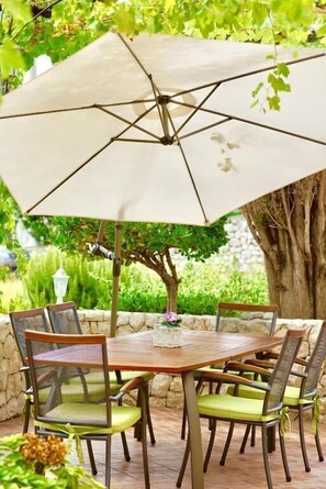 A round wooden table with six chairs, an umbrella, and a stone wall in the background. - Apartment Ljubica (Rab)