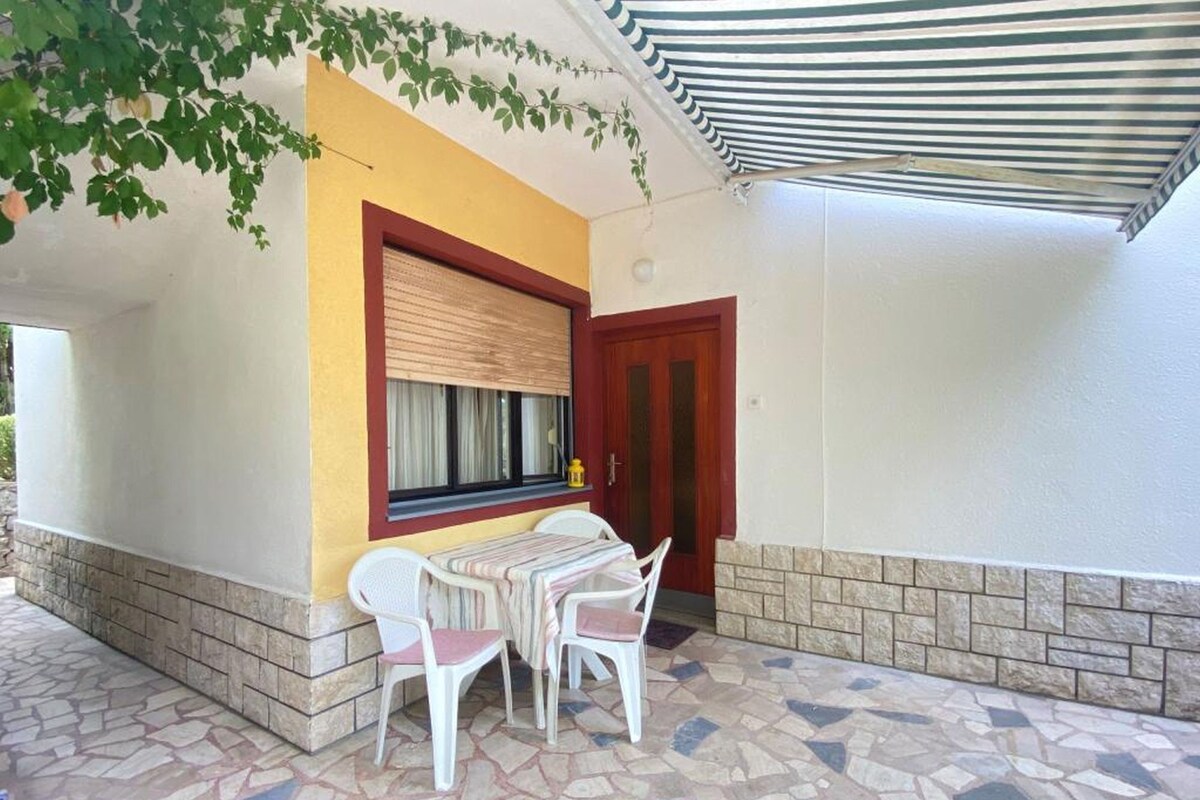 Eine Terrasse mit Tisch und Stühlen, ein Fenster mit Jalousie, eine Tür und ein Fliesenboden.
