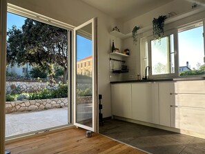 A modern kitchen with a sliding glass door leading to a stone wall garden, white cabinets, and a black countertop. - House Pavicic (Jelsa)