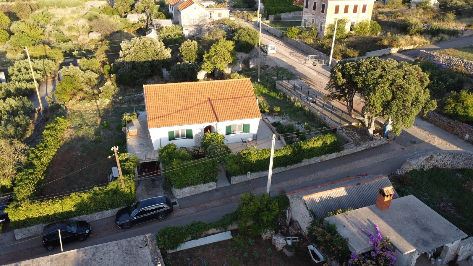 An aerial view of a residential area with a house featuring a tiled roof, a paved driveway, and a small garden.