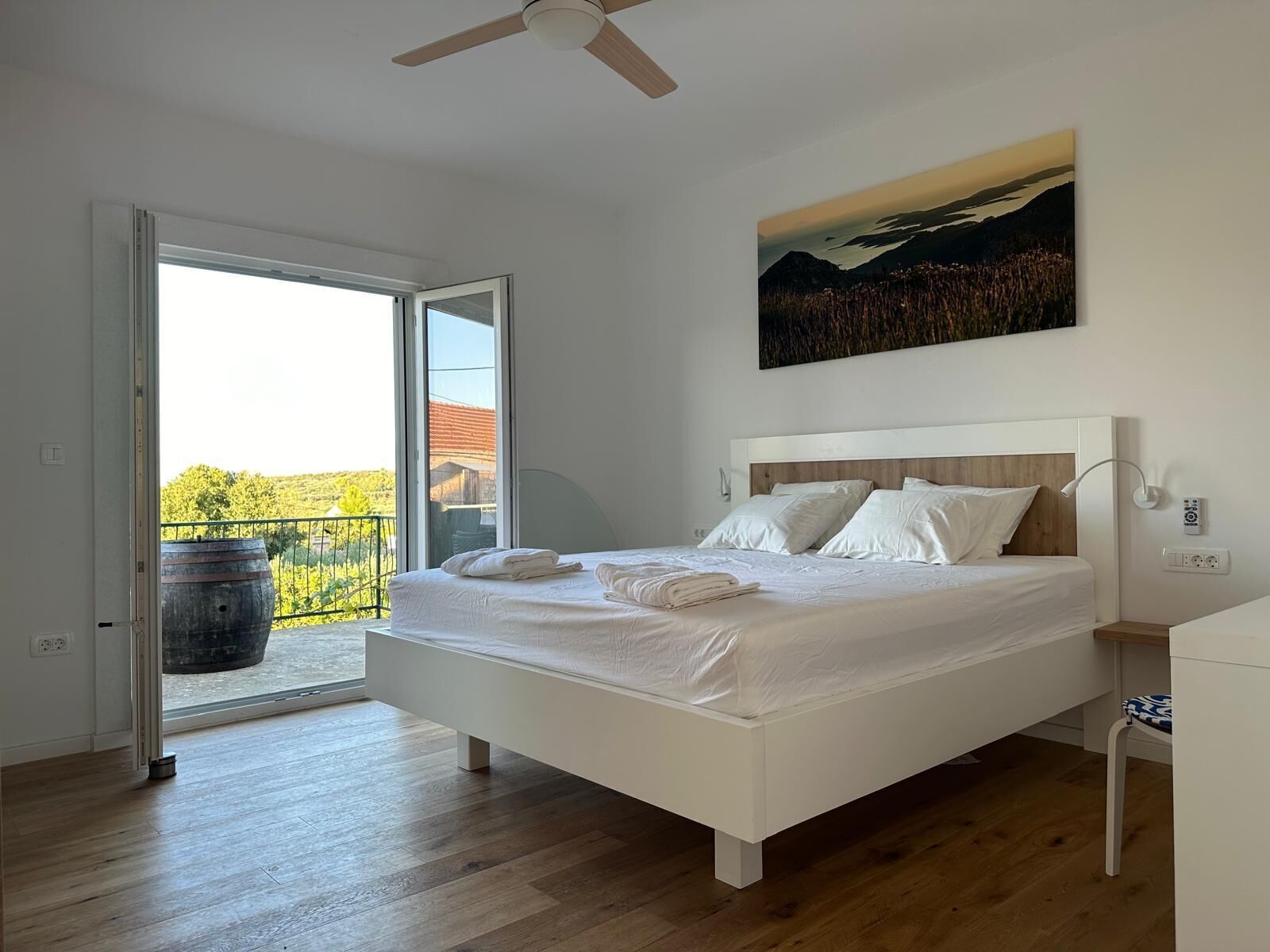 A bedroom with a bed, a painting, a ceiling fan, and a view through an open door.