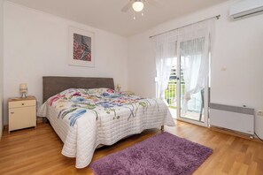 A bedroom with a bed, a nightstand, a window with curtains, a ceiling fan, and a radiator.